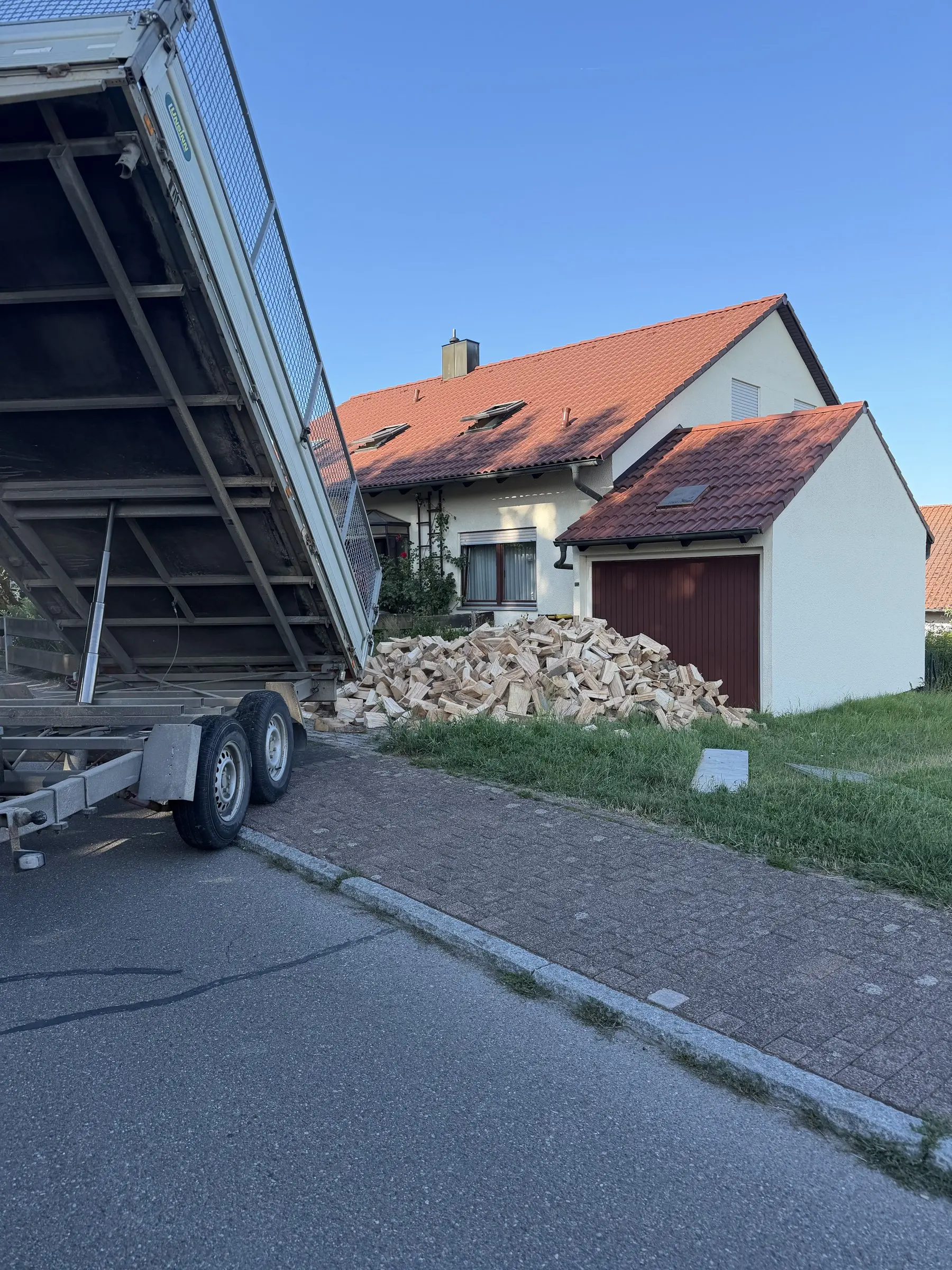 Kippanhänger von Alber Brennholz kippt Buchenholz vor einem Wohnhaus ab